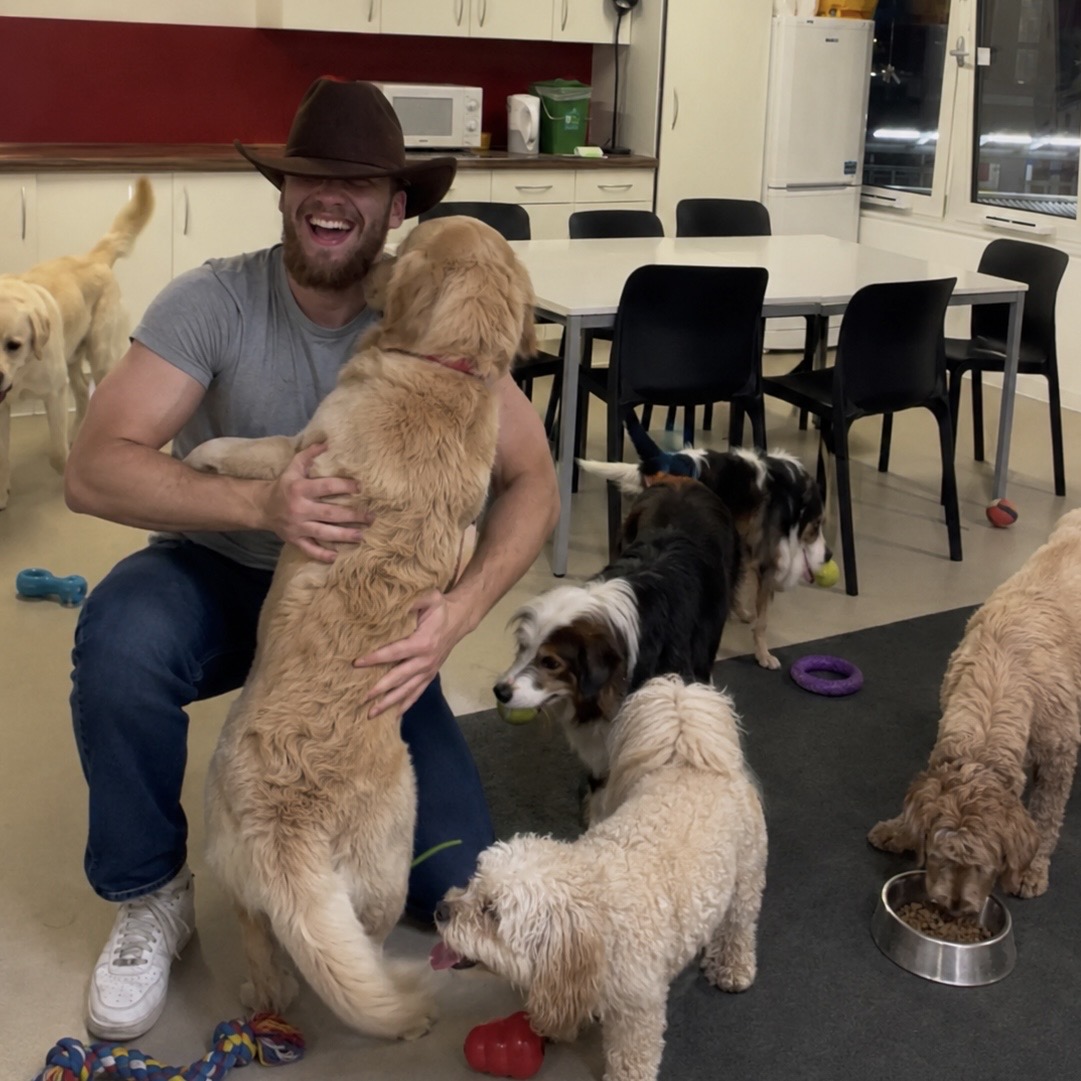 Michał in a cowboy hat, laughing while a golden retriever hugs him at daycare