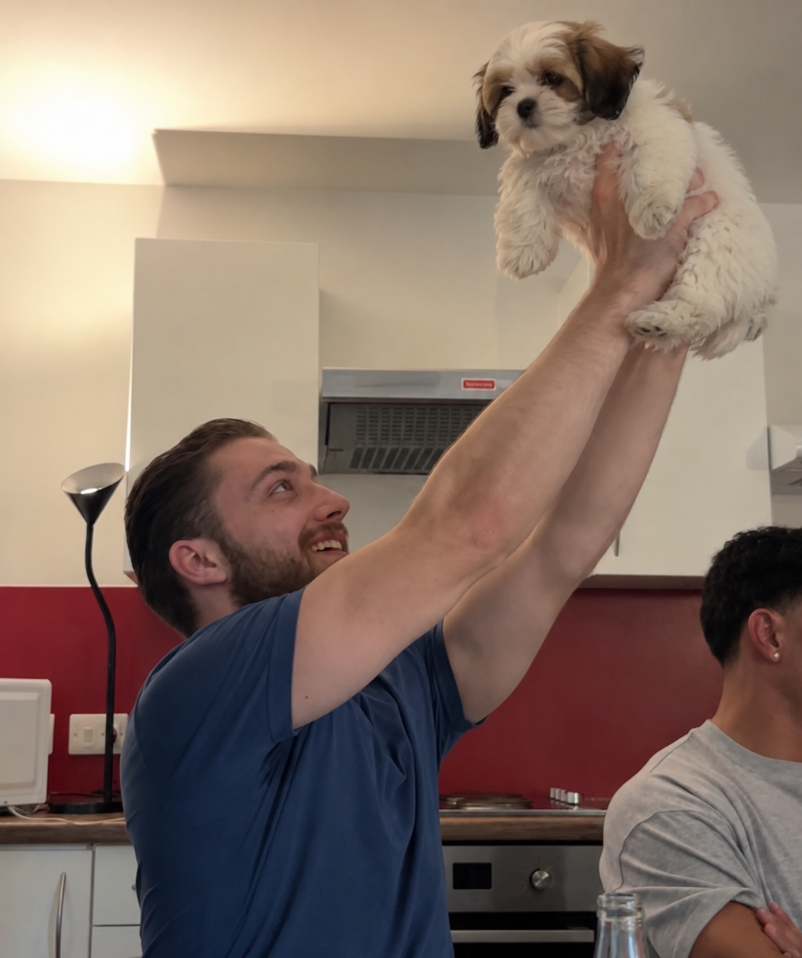 Michał lifting a fluffy shih tzu puppy in the air, both grinning